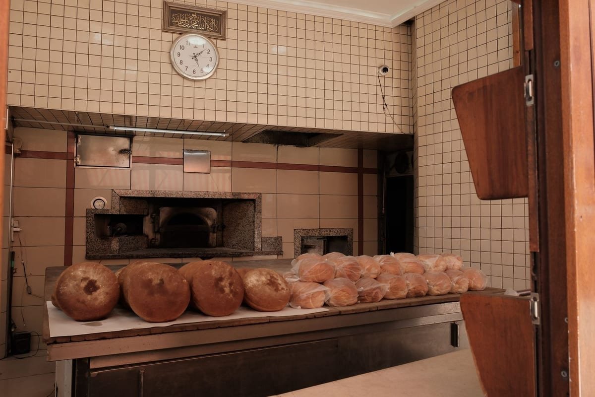 Padeiro tirando os pães do forno na cozinha da padaria
